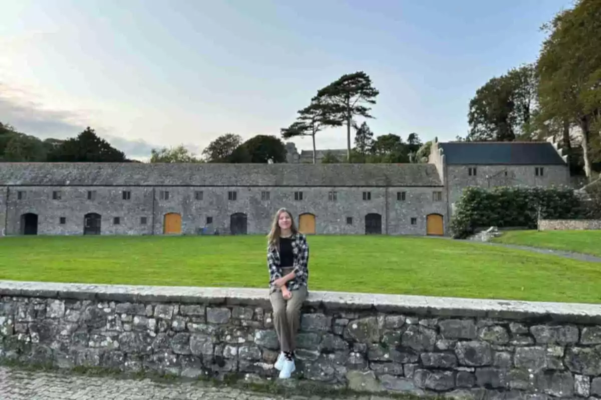 Infanta Sofía sitting on a stone wall in front of an old building with wooden doors and a wide green lawn. Infanta Sofía sitting on a stone wall in front of an old building with wooden doors and a wide green lawn.