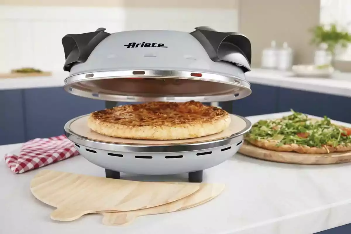A pizza cooking in an electric oven on a kitchen countertop, with an additional pizza topped with arugula in the background and a red and white checkered kitchen towel next to it. A pizza cooking in an electric oven on a kitchen countertop, with an additional pizza topped with arugula in the background and a red and white checkered kitchen towel next to it.