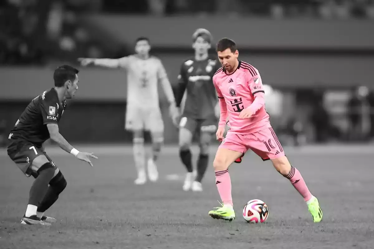 Un jugador de fútbol con uniforme rosa controla el balón mientras un oponente se acerca en un campo de juego.