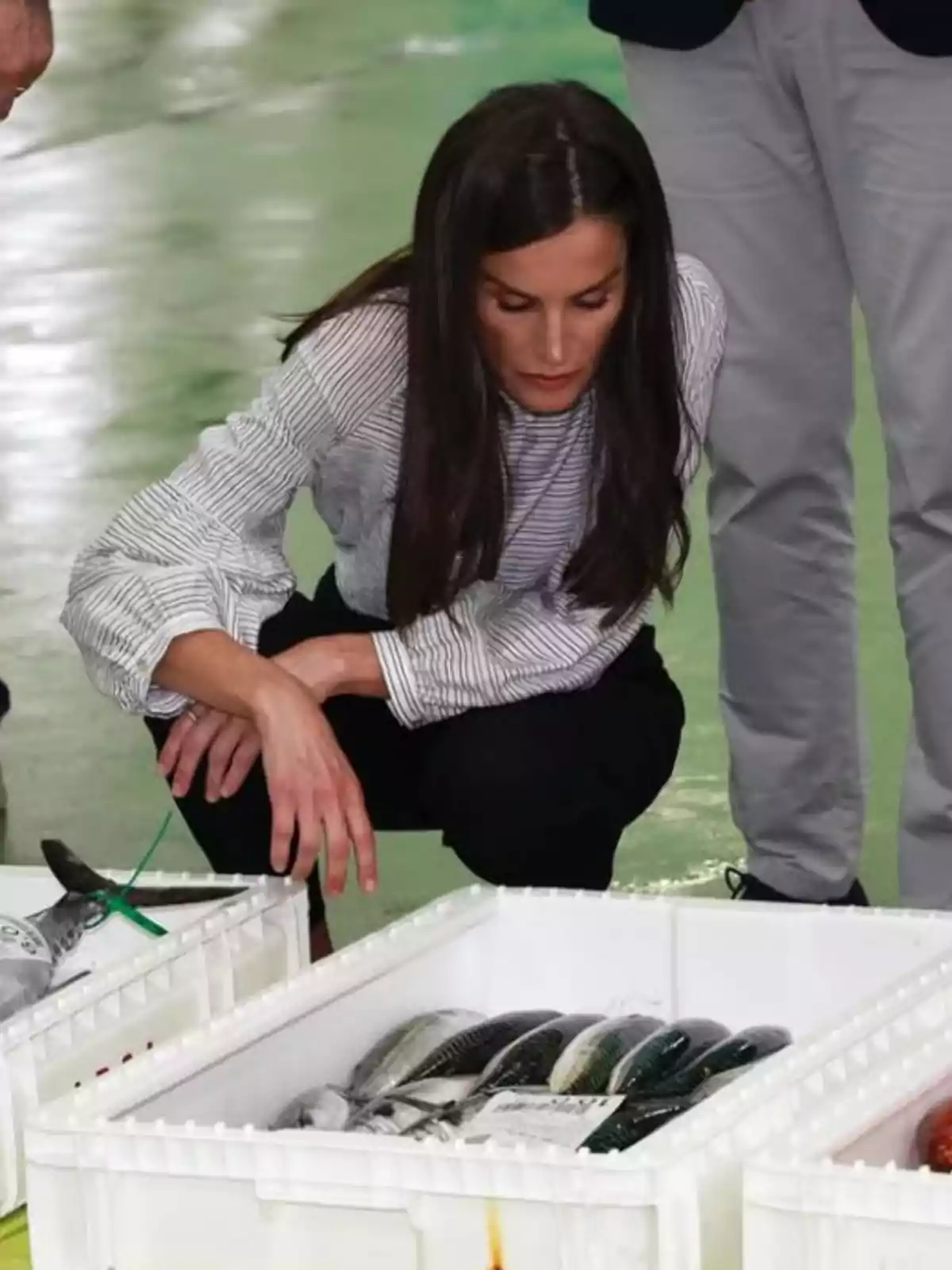 La reina Letizia observa atentamente una caja blanca llena de pescado fresco en un mercado o lonja