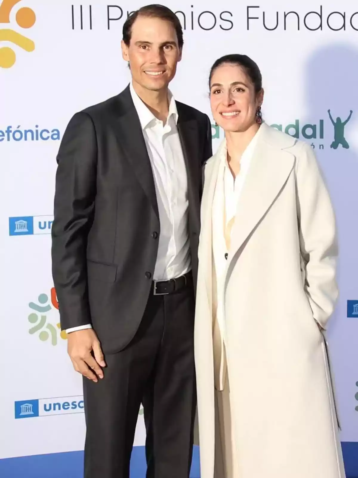 Rafa Nadal y Xisca Perelló posan juntas en un evento formal con un fondo que muestra logotipos de organizaciones. Rafa Nadal y Xisca Perelló posan juntas en un evento formal con un fondo que muestra logotipos de organizaciones.