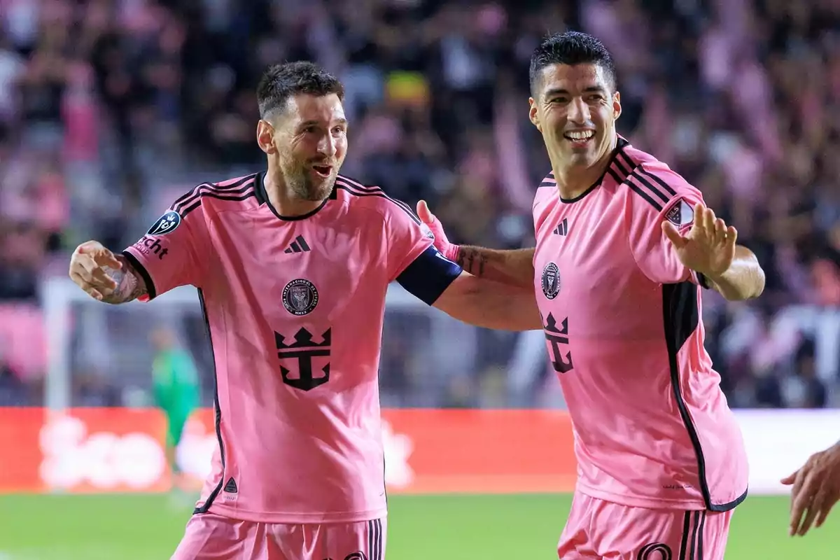 Dos futbolistas con uniforme rosa celebran en el campo de juego.